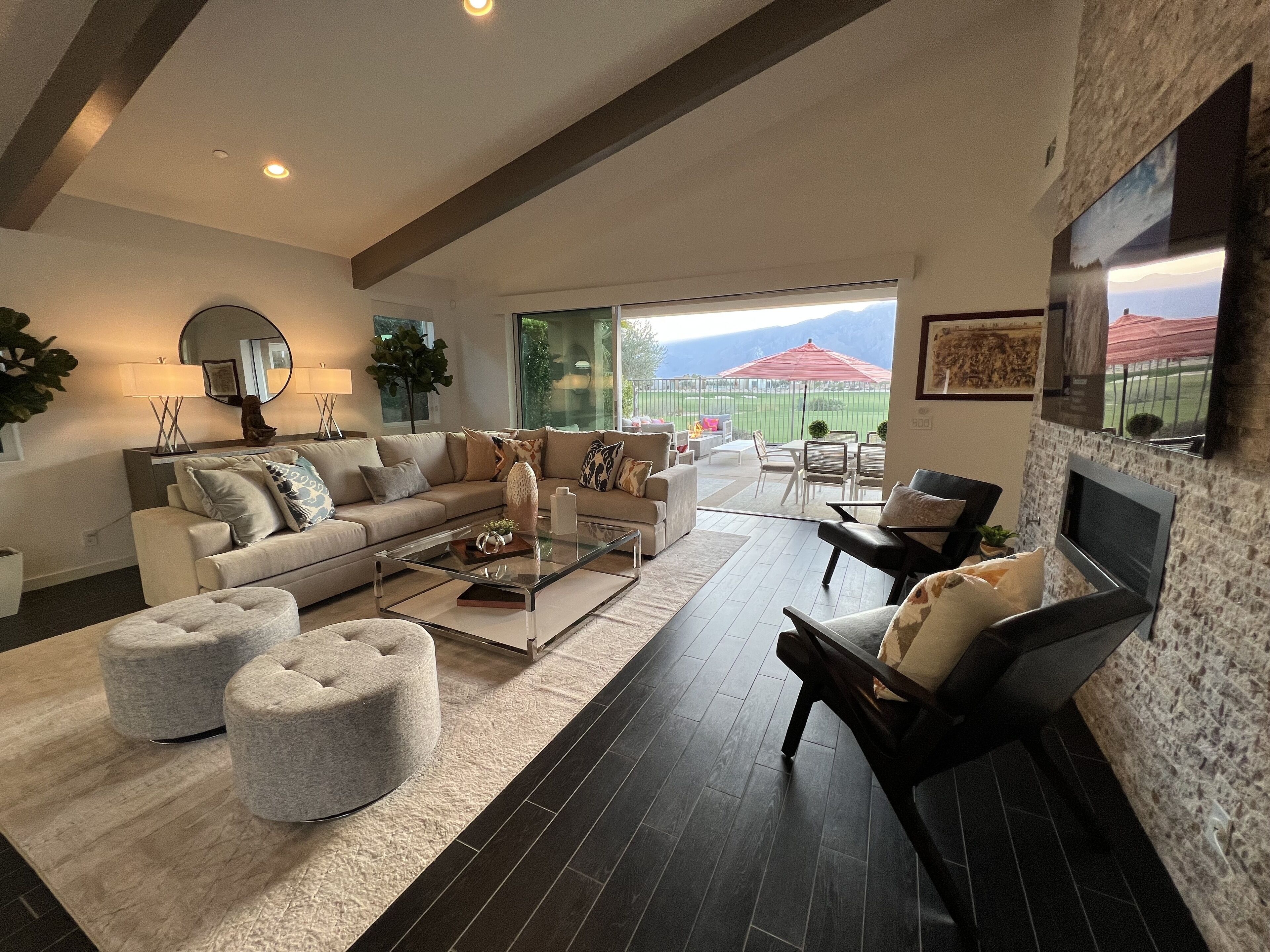 A spacious living room with a large sofa, ottomans, a coffee table, and a TV mounted on a stone wall.