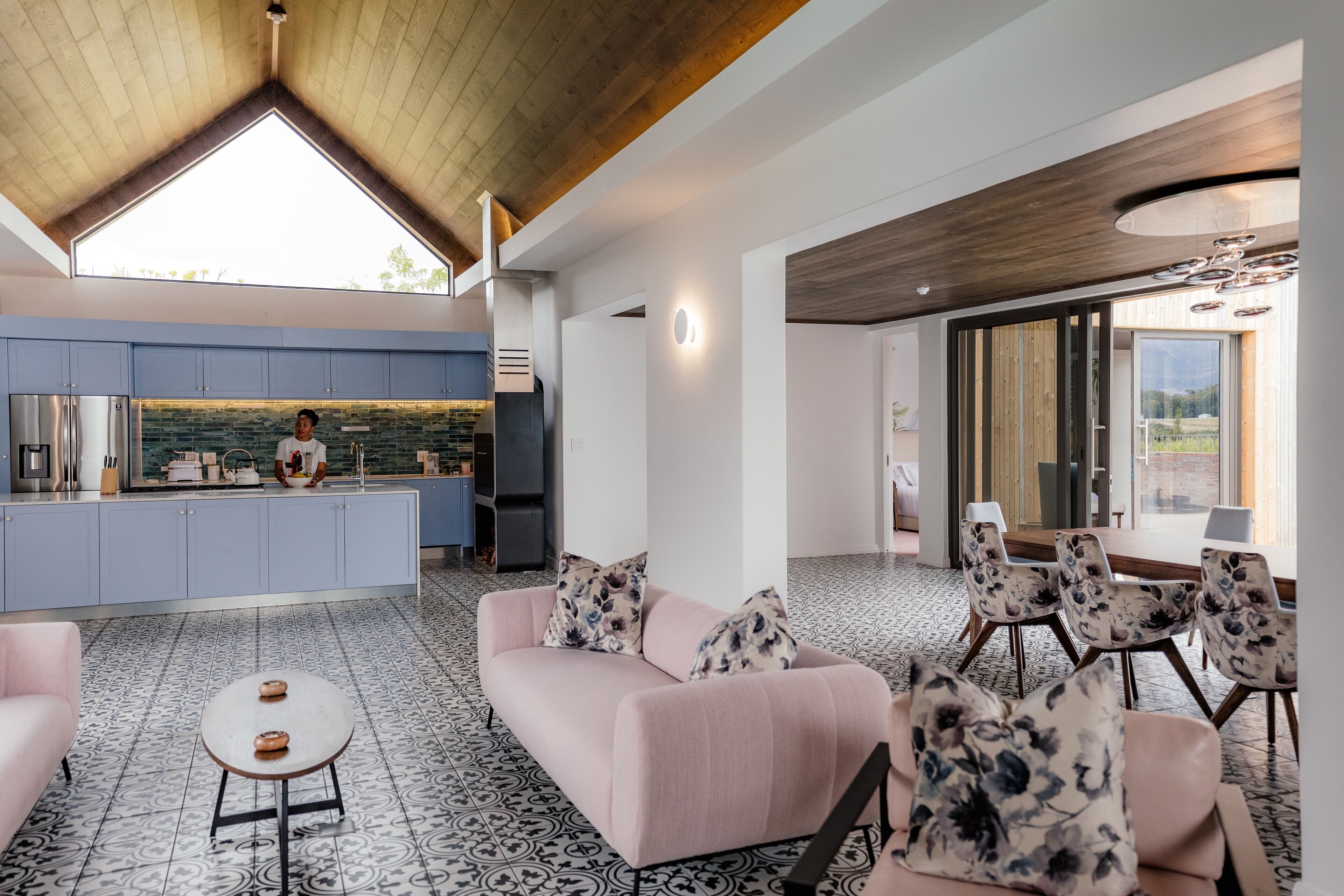 A modern kitchen with a chef, a dining area with a large table and chairs, and a cozy seating area with a sofa and coffee table.