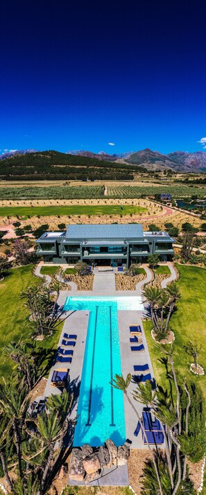 A modern hotel with a swimming pool, sun loungers, and a view of mountains. - Ludus Magnus (Franschhoek)