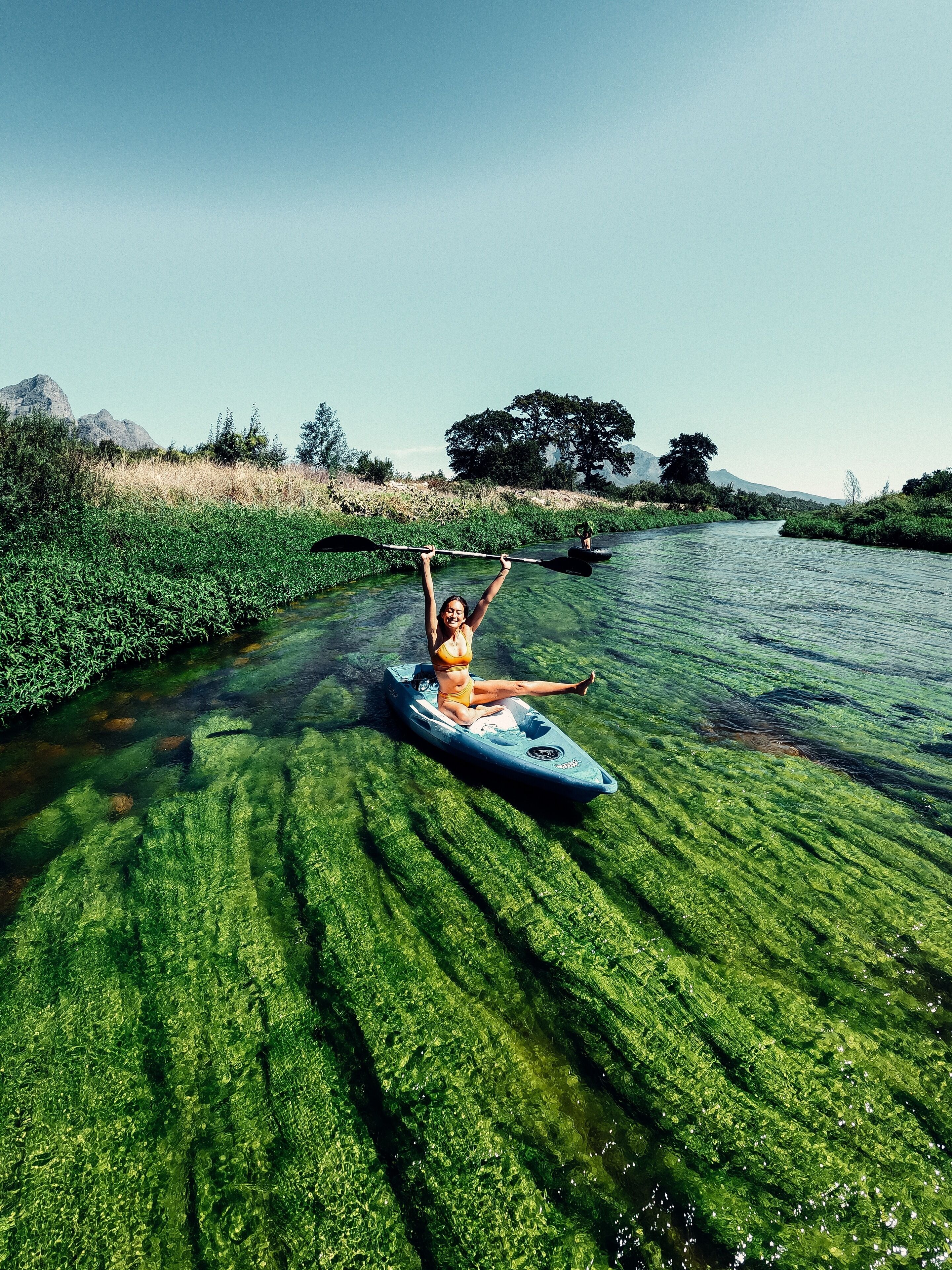 A person kayaking on a river surrounded by greenery and trees.