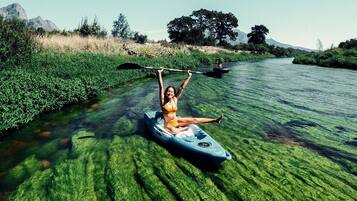 A person kayaking on a river surrounded by greenery and trees.