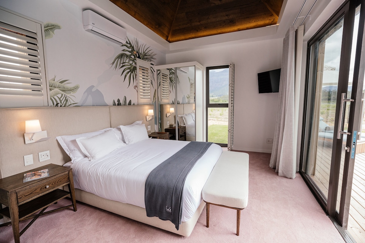 Ein Schlafzimmer mit Bett, Nachttischen, einer Bank, einem Fernseher und einem großen Fenster mit Blick.