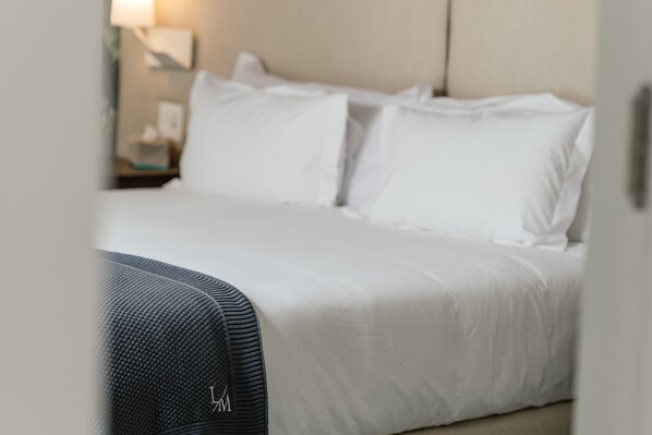 Een net opgemaakt bed met witte lakens en een donker gestreept dekbed.