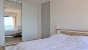 Een slaapkamer met een bed, een kledingkast en een spiegel die een balkon met uitzicht weerkaatst.
