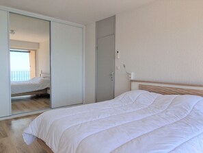 Un dormitorio con cama, armario y espejo que refleja un balcón con vistas.