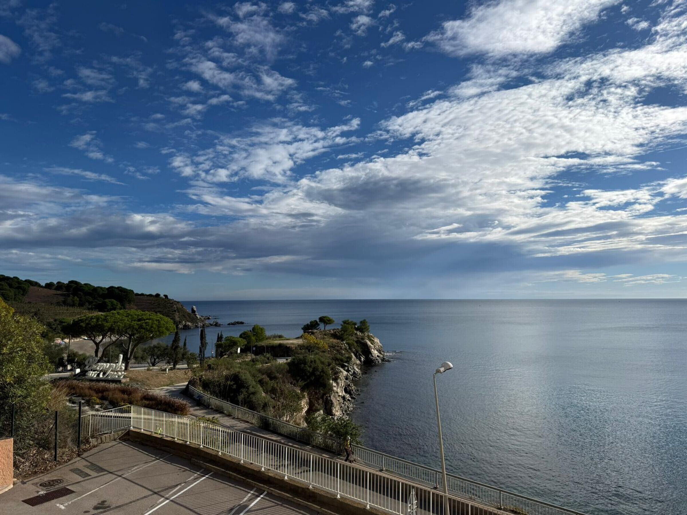 A coastal view with a paved walkway, a railing, and a clear sky.