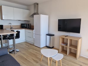 A modern kitchen with white cabinets, a stainless steel range hood, a white refrigerator, a microwave, a sink, and a flat-screen TV mounted on the wall. - BANYULS-SUR-MER: T3 Apartment with Air Conditioning, Near Beach (Banyuls-sur-Mer)