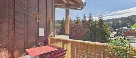 Un balcon en bois avec une table et des chaises rouges, une vue sur la ville et une enseigne accrochée au mur.