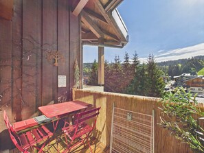 Ein hölzerner Balkon mit einem roten Tisch und Stühlen, Blick auf eine Stadt und ein Schild an der Wand.