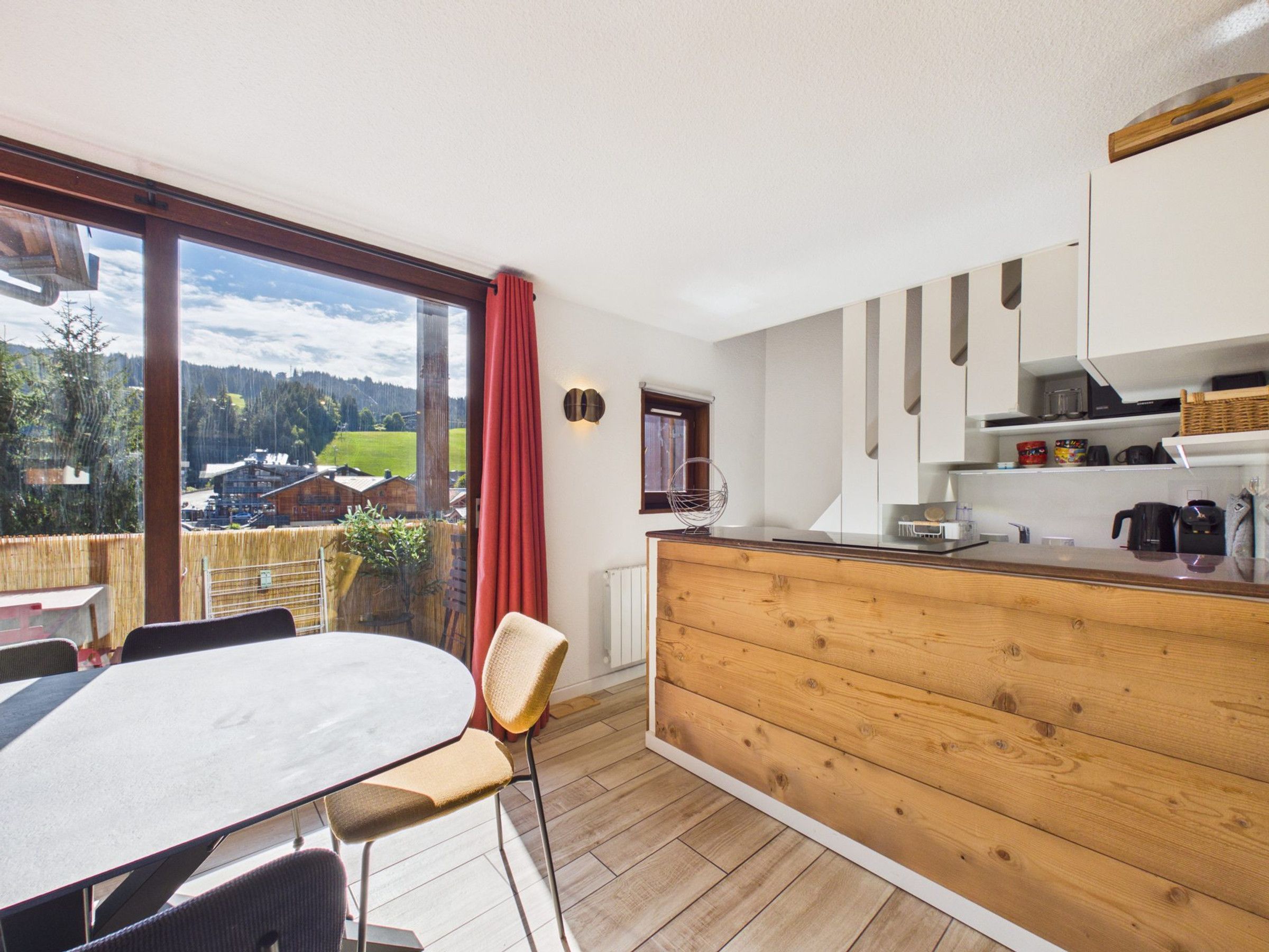 Una cocina moderna con encimera de madera, una zona de comedor con mesa y sillas, y un gran ventanal con vistas a un área boscosa.