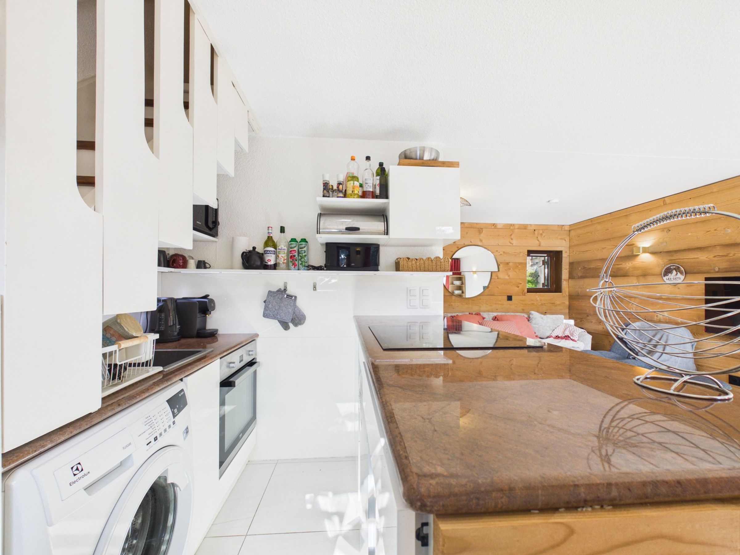 Une cuisine moderne dotée d’un lave-linge encastré, de meubles en bois et d’une chaise suspendue.