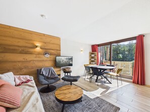 Un salon moderne avec un mur en bois, une table basse ronde, un canapé et un coin repas comprenant une table et des chaises.