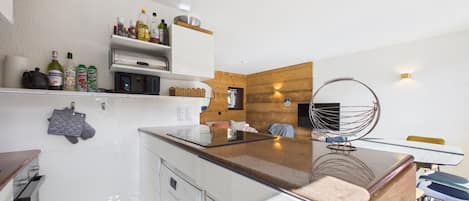 A modern kitchen with white cabinetry, a wooden accent wall, and a dining area with a hanging chair.