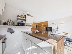A modern kitchen with white cabinetry, a wooden accent wall, and a dining area with a hanging chair.