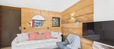 Una sala de estar moderna con un panel de madera, un espejo redondo, un sofá con cojines, una mesa de centro y un televisor.