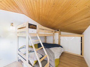 Ein Schlafraum mit Etagenbetten, Holzbalkendecke und weißen Wänden.