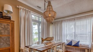Ruokailutila, jossa on puinen pöytä, valkoiset tuolit, kattokruunu ja suuret ikkunat, joissa on valkoiset verhot.