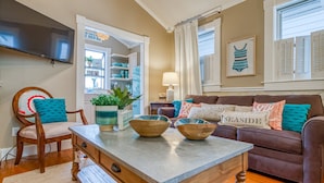 A cozy living room with a wooden coffee table, a brown sofa, and a television mounted on the wall. - Perfect Couples Getaway, Heated Pool Access (Tybee Island)