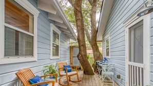 A wooden deck with rocking chairs and a table, surrounded by blue siding and large trees. - Perfect Couples Getaway, Heated Pool Access (Tybee Island)