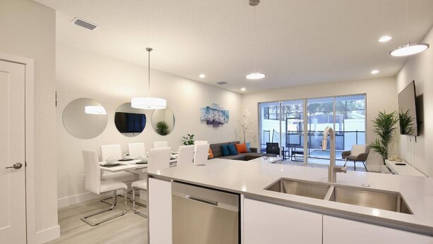 A modern kitchen with a central island, white cabinetry, and a dining area with a sofa and chairs. - Amazing NEW 3 bedroom+loft townhouse in Hidden Forest, with private pool! (Clermont)
