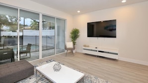 A modern living room with a flat-screen TV, a glass sliding door leading to a balcony, and a minimalist design. - Amazing NEW 3 bedroom+loft townhouse in Hidden Forest, with private pool! (Clermont)