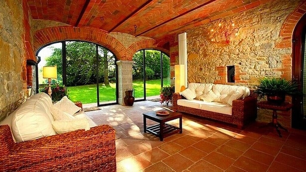 Un salón espacioso con pared de piedra, un gran ventanal arqueado y un sofá de mimbre.