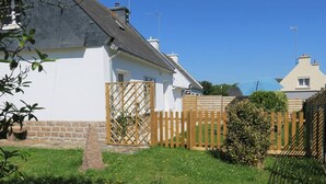 Ein Wohnhaus mit weißen Wänden, einem Holzzaun und einem Garten mit Gras und Blumen.