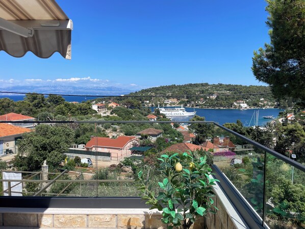 A balcony with a view of a coastal town, a ship named 'KOROLINJA,' and a statue.