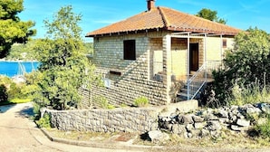 A stone house with a tiled roof, a porch, and a staircase leading to the entrance.