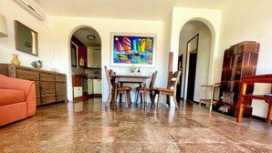 Un vaste espace de vie comprenant une table à manger et des chaises, une cuisine à l’arrière-plan et un tableau coloré accroché au mur.