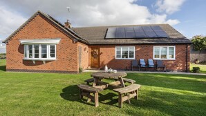 Une maison en briques avec un toit équipé de panneaux solaires, une table de pique-nique et un petit jardin.