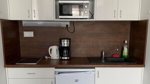 Une petite cuisine équipée d’un four à micro-ondes, d’une machine à café, d’un évier et d’un petit réfrigérateur.