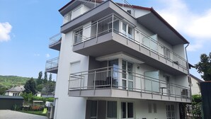 Un immeuble à plusieurs étages doté de balcons, d’un espace extérieur couvert aménagé en coin salon et d’une pelouse artificielle verte.
