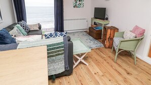 A cozy living room with a sofa, a small table, a chair, a television, and a view of the sea. - Sea Snug (Berwick-upon-Tweed)