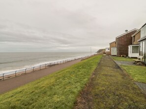 A coastal walkway with a grassy path leading to a building with a brick facade. - Sea Snug (Berwick-upon-Tweed)