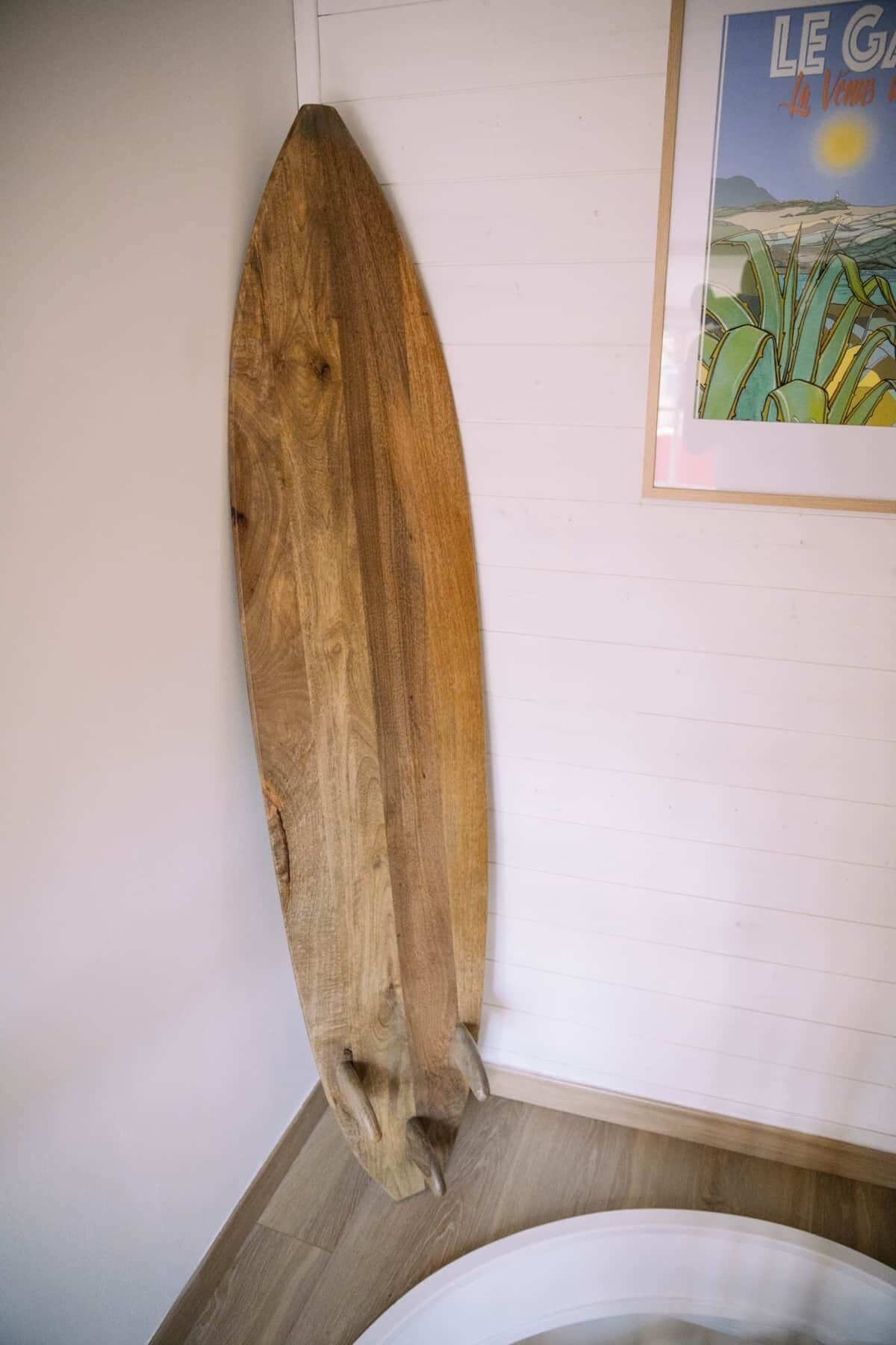 Ein Holzsurfbrett lehnt an einer Wand in einem Zimmer mit einem Poster mit Strandmotiv.