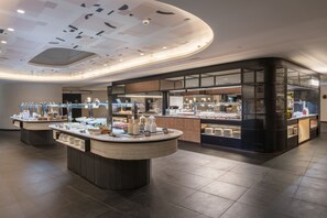 Eine moderne Hotelhalle mit einer zentralen Rezeption, einem Buffetbereich und einer Sitzecke mit gewölbter Decke.