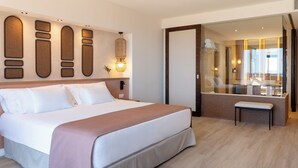 Une chambre d’hôtel avec un grand lit, un banc, un miroir et une vue sur le hall d’entrée.