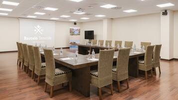 Un salón de conferencias con una larga mesa, sillas de mimbre y una pantalla proyectora mostrando 'Barceló Tenerife'.