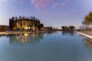Ein Swimmingpool mit Liegestühlen und Sonnenschirmen, umgeben von einem modernen Gebäude mit Holzfassade und Grünflächen.