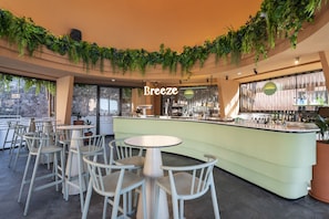 Eine Bar mit einem hellgrünen Tresen, weißen Stühlen und hängenden Pflanzen.