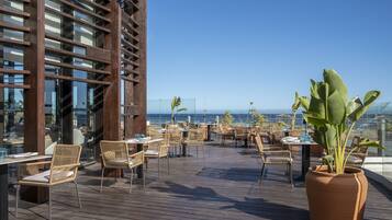 Enjoy ocean views from this outdoor dining area with wicker chairs and a large potted plant.