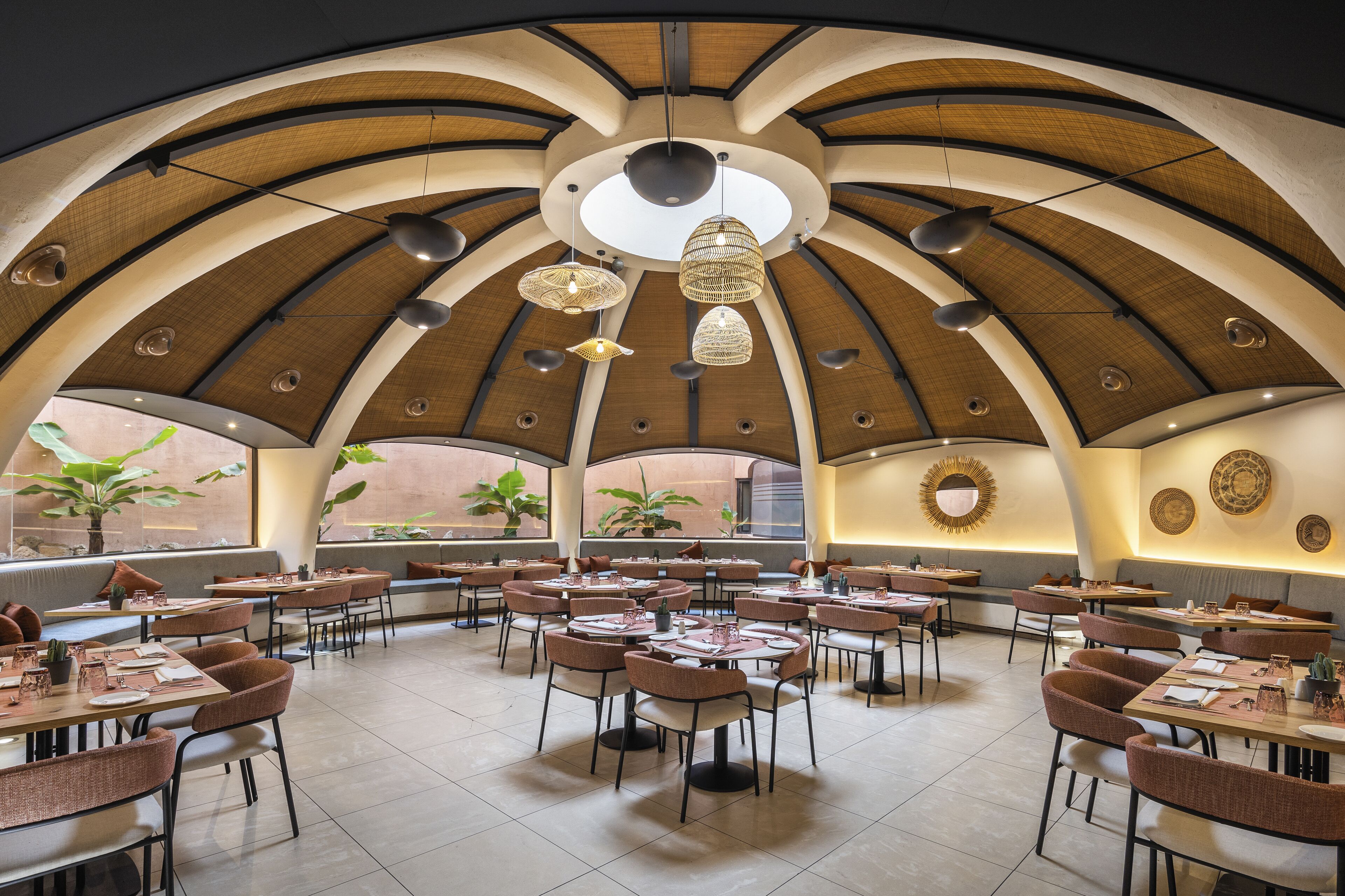 Un vaste espace dédié à la salle à manger, avec de nombreuses tables et chaises, un haut plafond en arc de cercle et de grandes fenêtres laissant entrer la lumière naturelle.