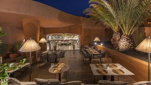 Un espace de restauration en plein air avec des tables et des chaises, un bar en arrière-plan et des palmiers.