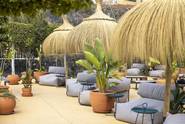 An outdoor seating area with cushioned sofas, round tables, and potted plants.