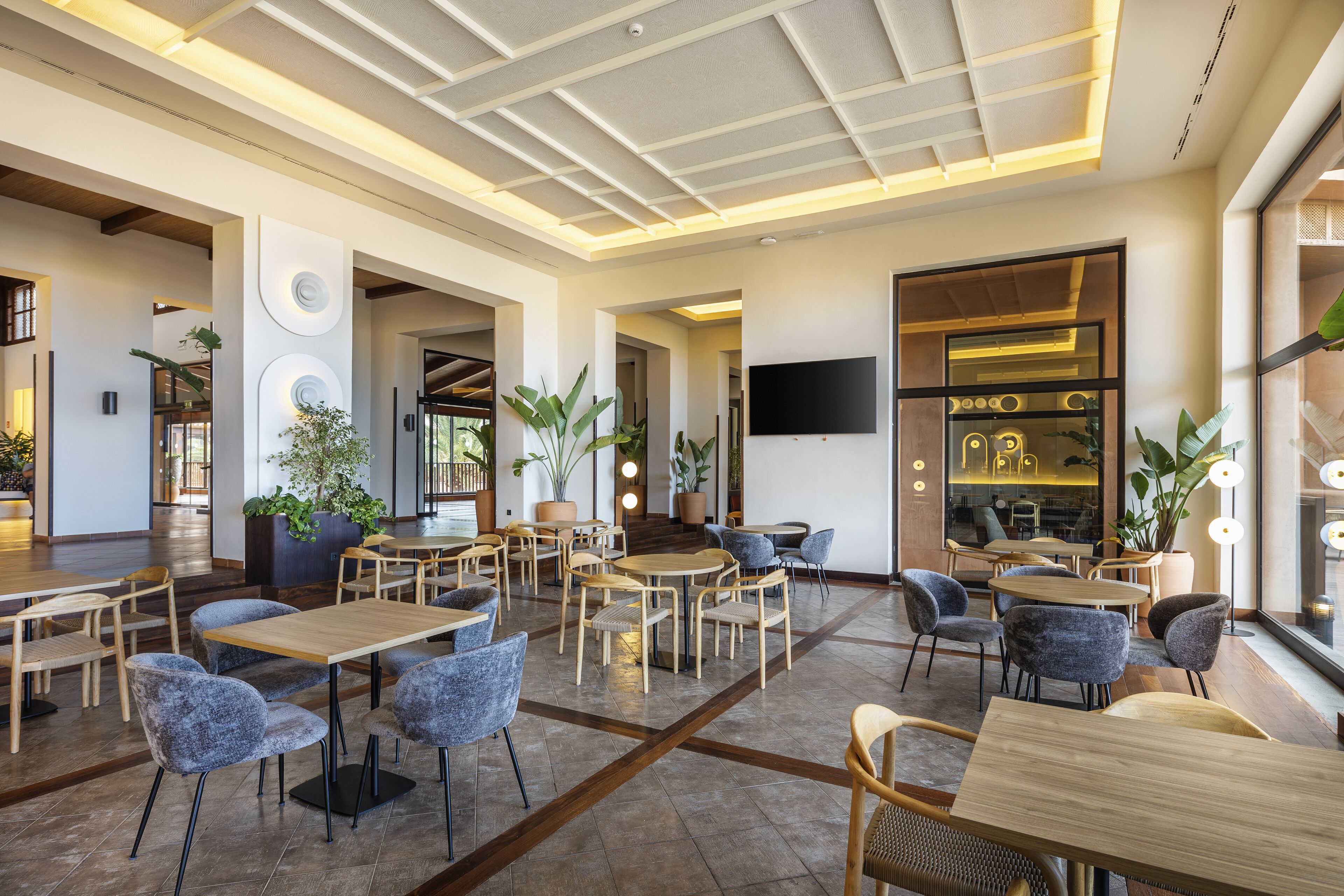 Un restaurante moderno con mesas y sillas de madera, plantas en macetas y un televisor de pantalla plana en la pared.