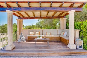 Un espace extérieur abrité, aménagé avec un banc, une statue et une table agrémentée de plantes.