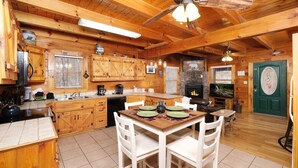 A wooden cabin interior with a dining area, kitchen, and a green door. - 1BR-hot tub-pool table-close to Dollywood (1 free ticket)! (Sevierville)