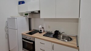Cocina compacta con refrigerador, horno, lavaplatos y cafetera.