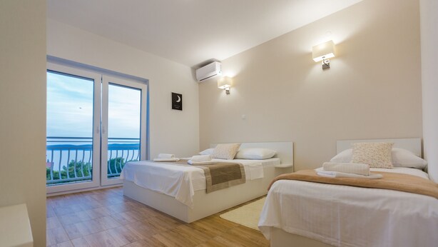 Habitación de hotel con dos camas, un balcón con vista al mar y un ventilador de techo.